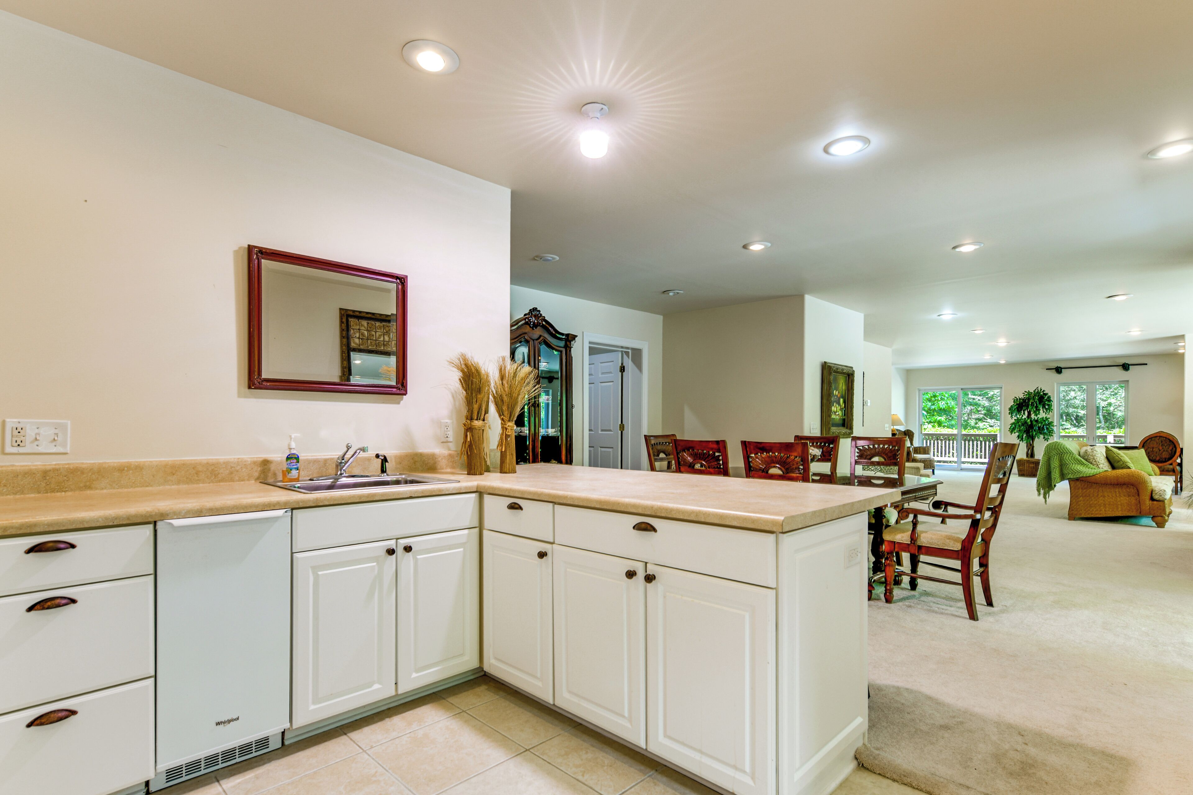 A kitchen with white cabinets, a sink, and a mirror. There is a dining area with a table and chairs.