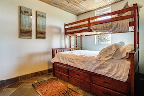 Ein Stockbett mit Holzrahmen, einer gesteppten Bettdecke und einem gemusterten Teppich auf Fliesenboden.