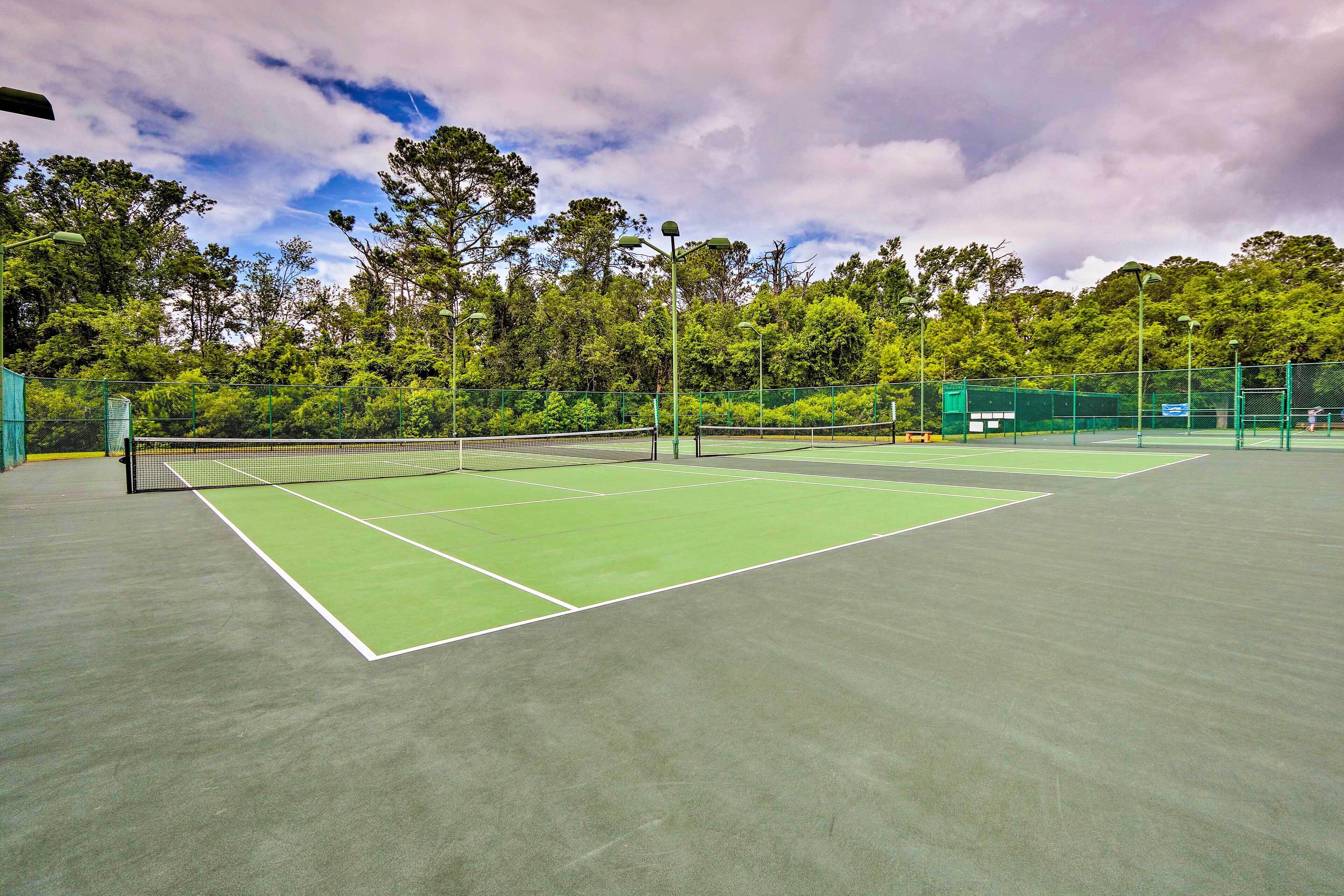 A tennis court with a green surface, surrounded by trees and a fence.
