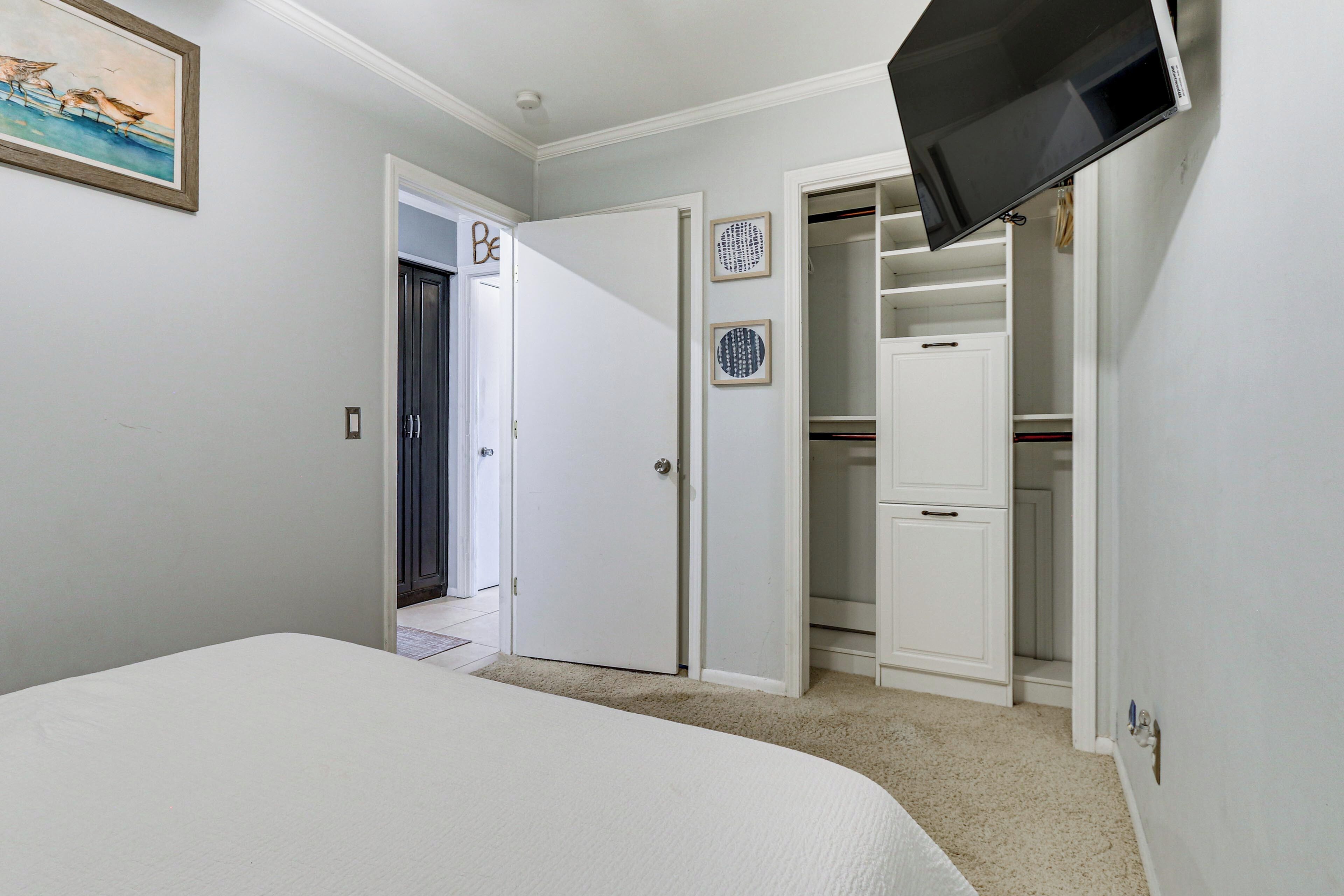 A bedroom with a bed, a TV mounted on the wall, a closet, and a door leading to another room.
