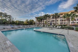 Piscina com espreguiçadeiras e um edifício ao fundo.