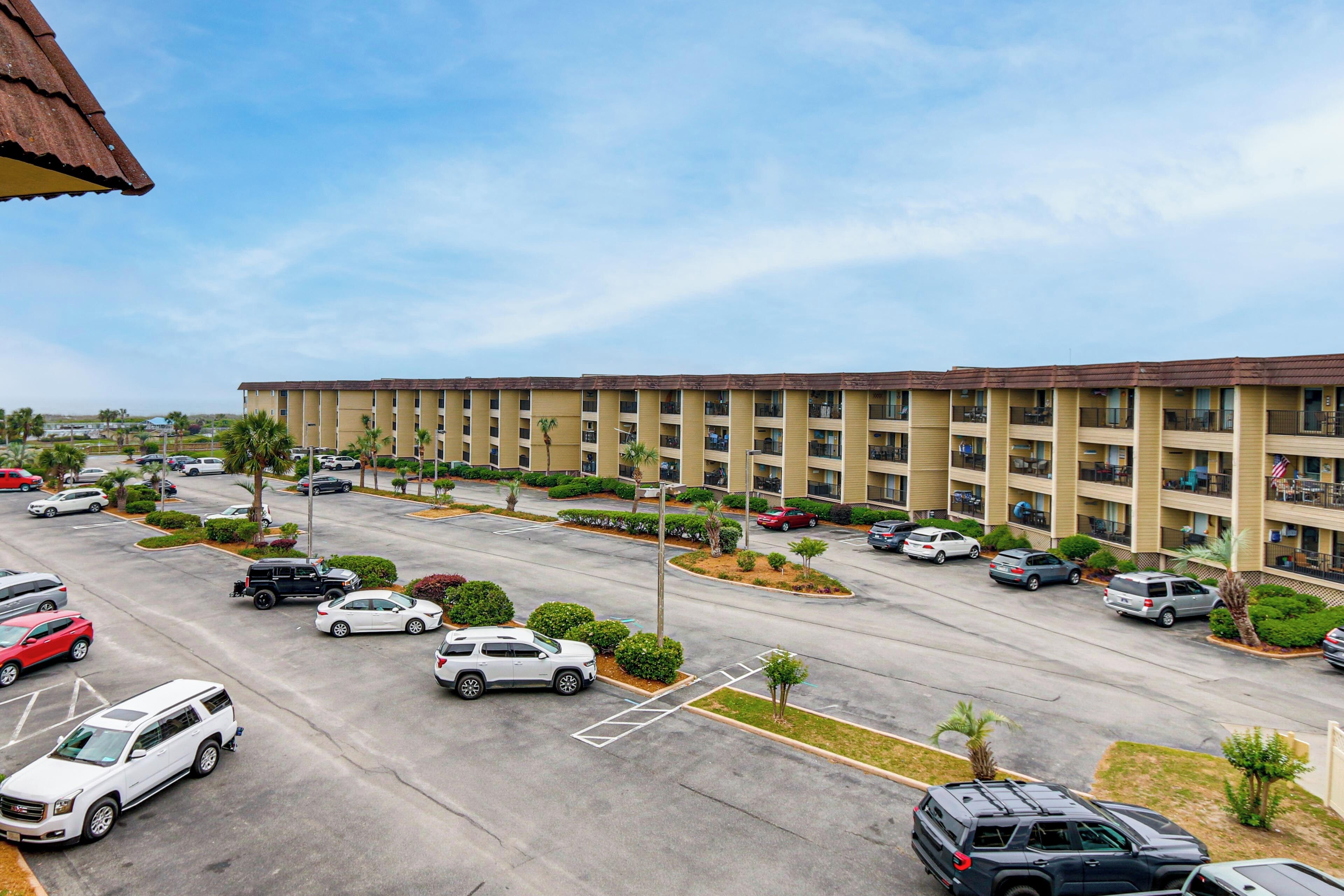 A multi-story hotel with a parking lot, several cars, and palm trees.