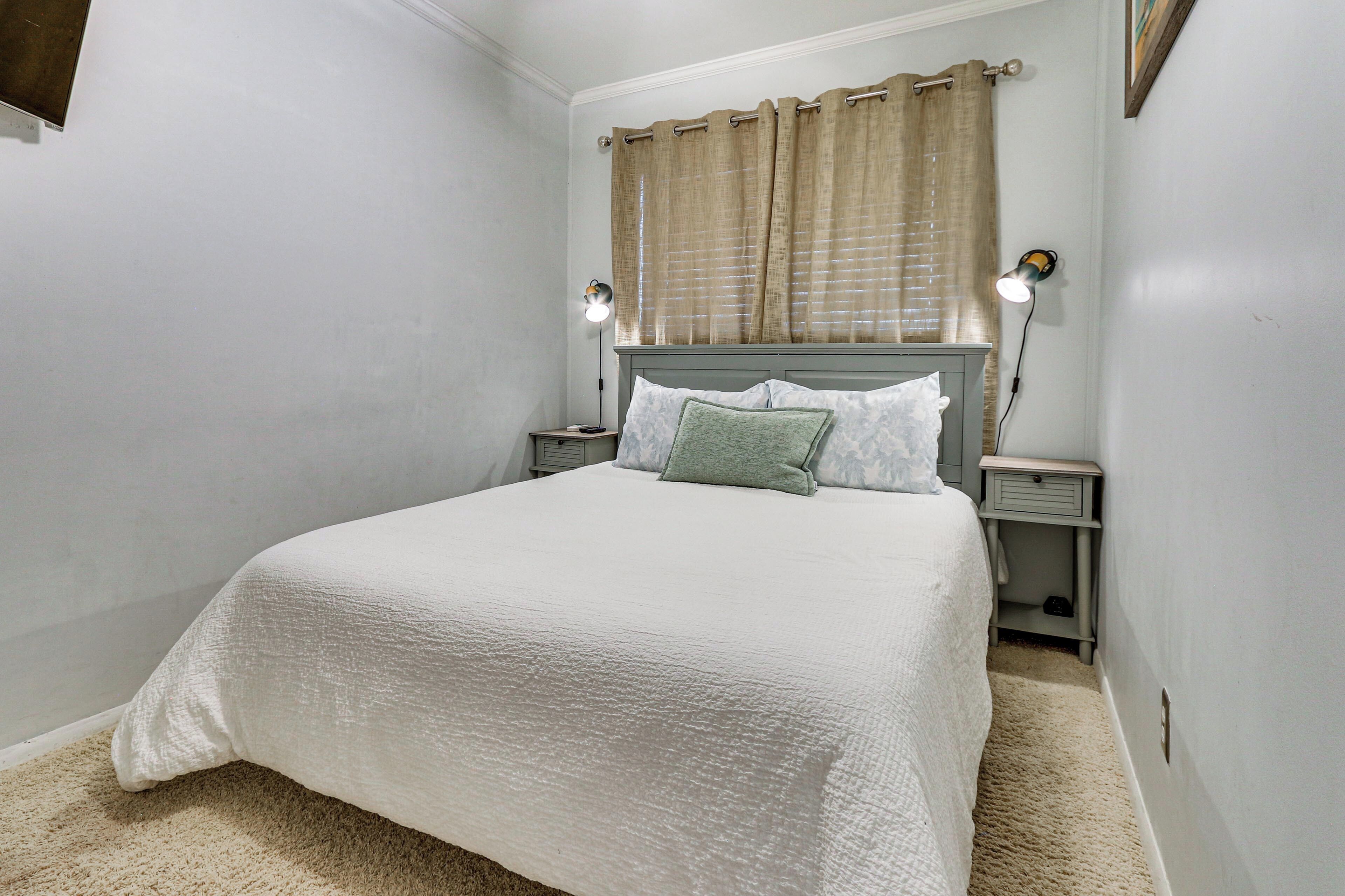 A bedroom with a bed, two bedside tables, a nightstand, a lamp, and a window with curtains.