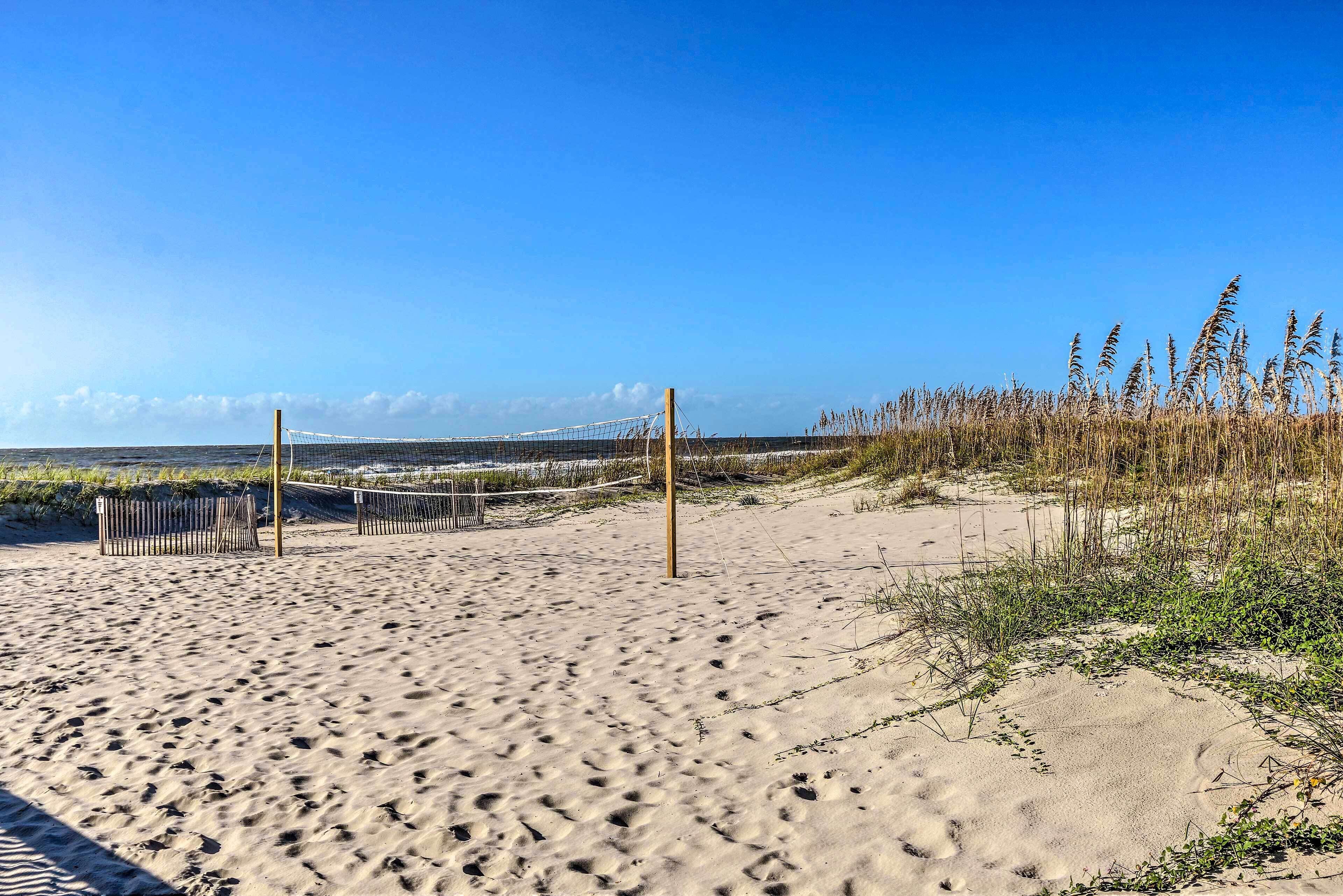 A sandy beach with footprints, a volleyball net, and tall grasses.