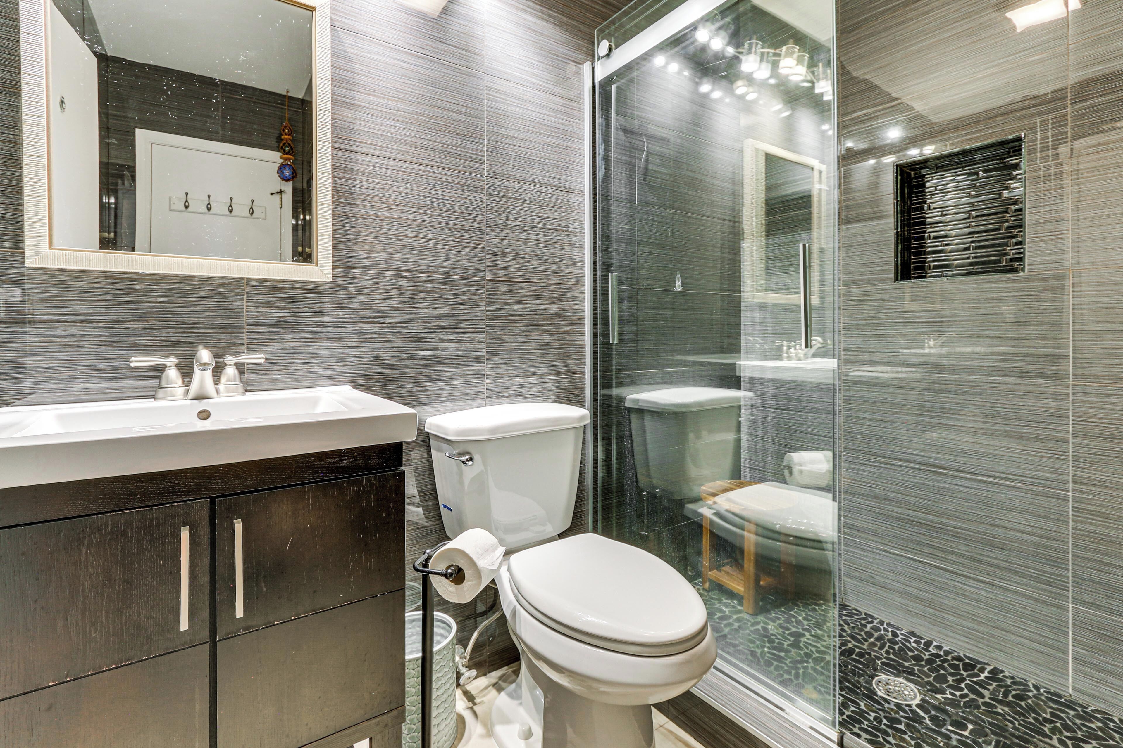 Une salle de bain moderne avec une douche à parois de verre, des toilettes et un lavabo surmonté d’un miroir.