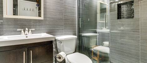 Une salle de bain moderne avec une douche à parois de verre, des toilettes et un lavabo surmonté d’un miroir.