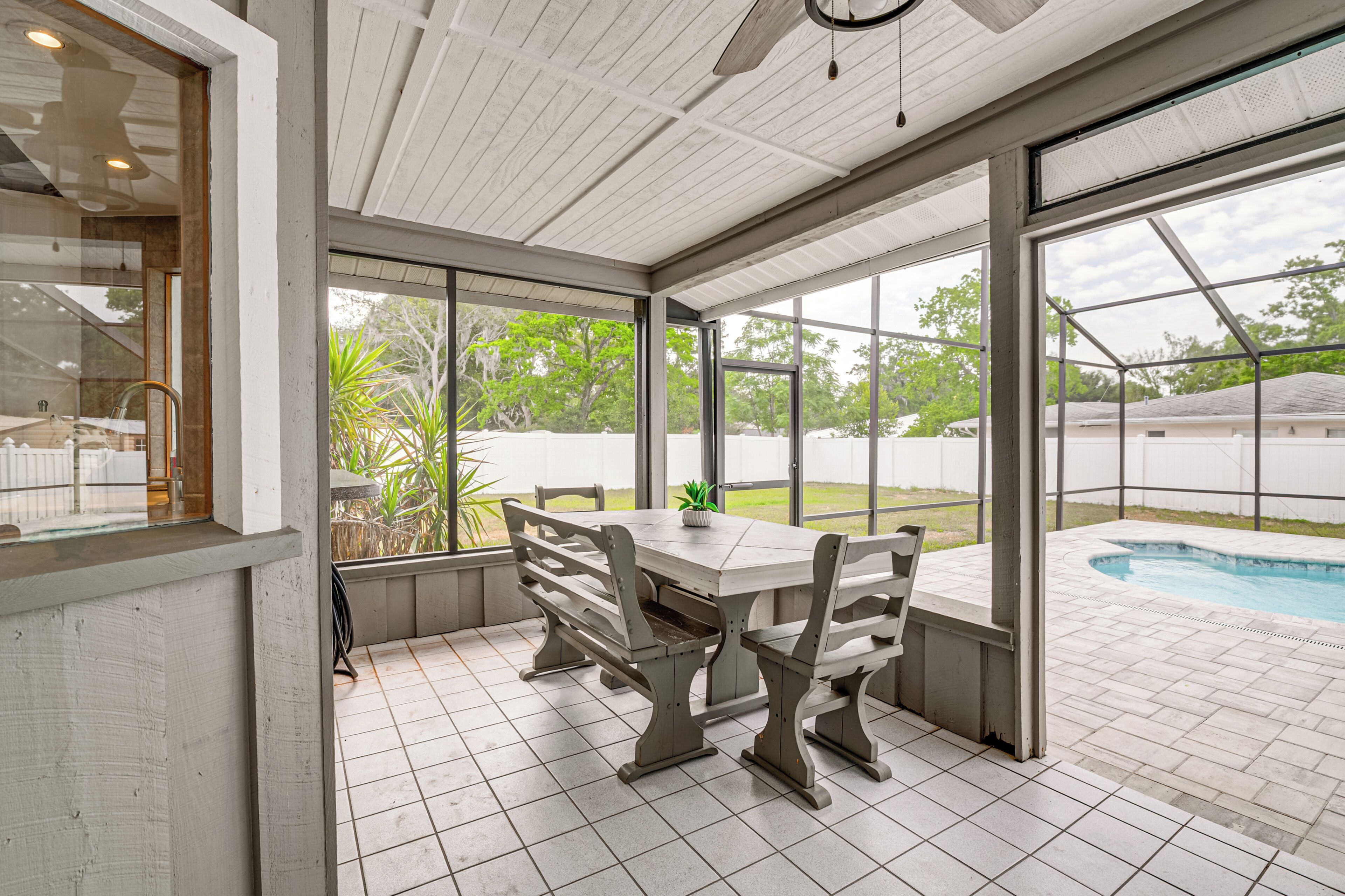 A covered patio area with a table and benches, large windows, and a view of a swimming pool.