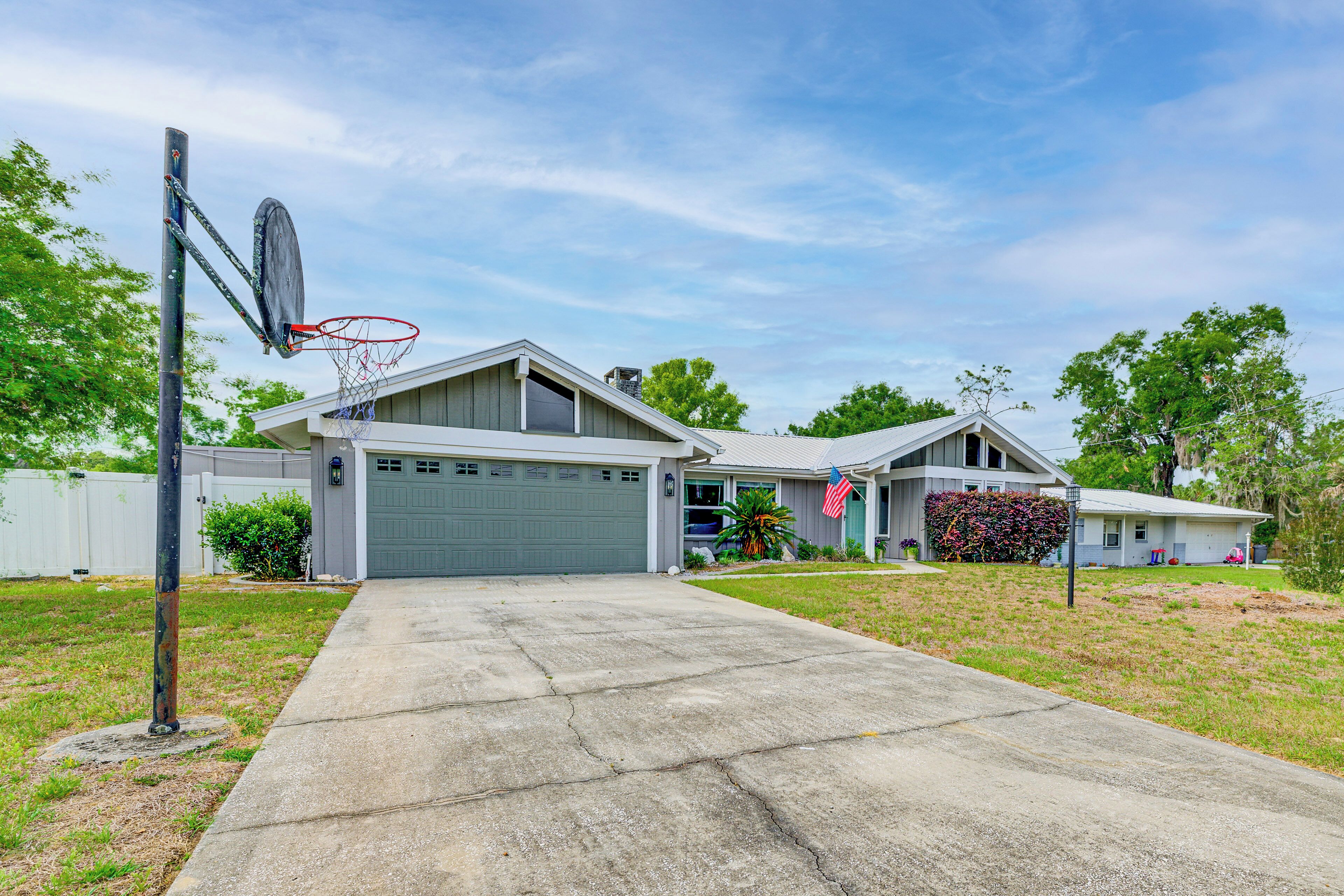 Une maison d’habitation avec un garage, un panier de basketball, une allée et une pelouse bien entretenue.