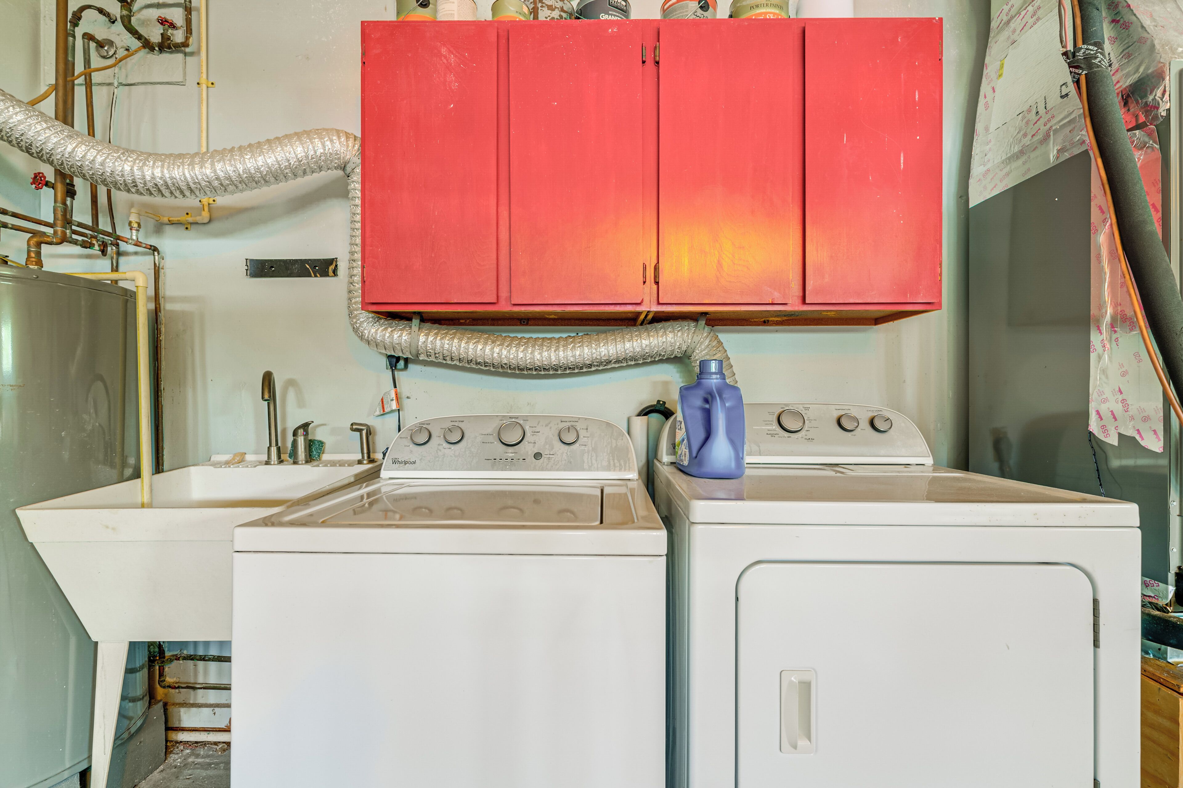 Un área de lavandería con lavadora, secadora, lavabo y un armario rojo arriba.