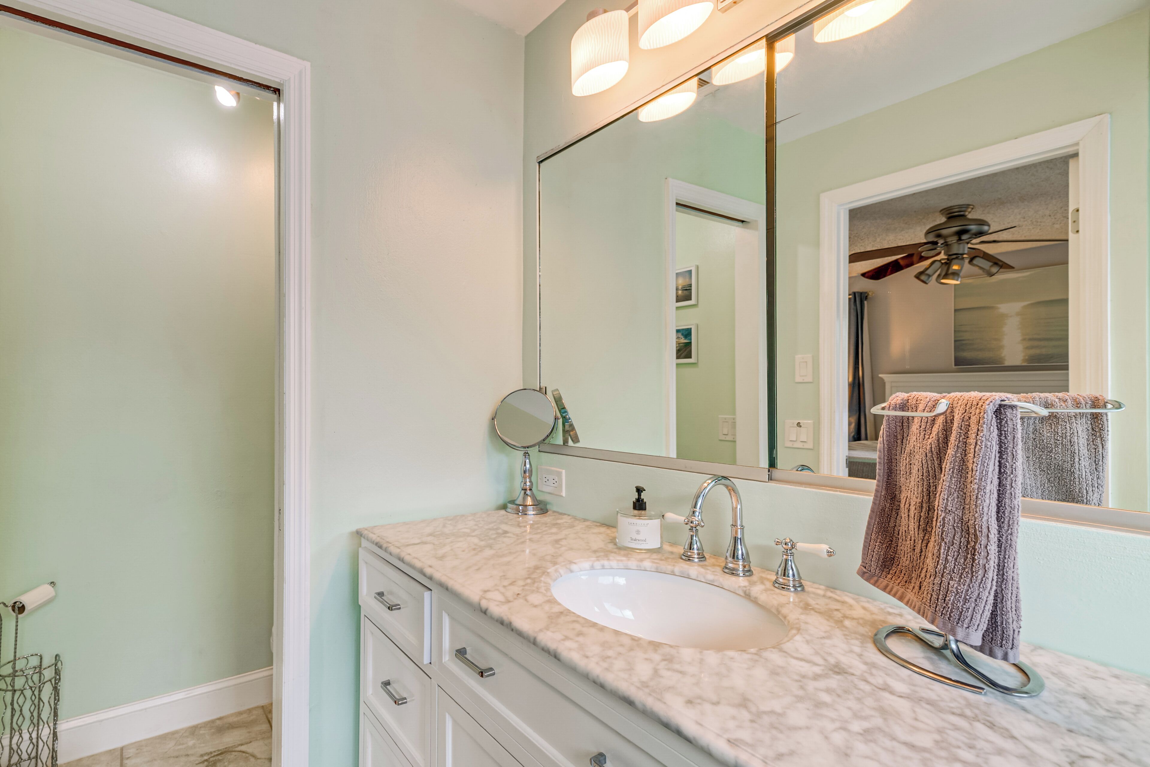 A bathroom with a marble sink, a mirror, a towel rack, and a ceiling fan.