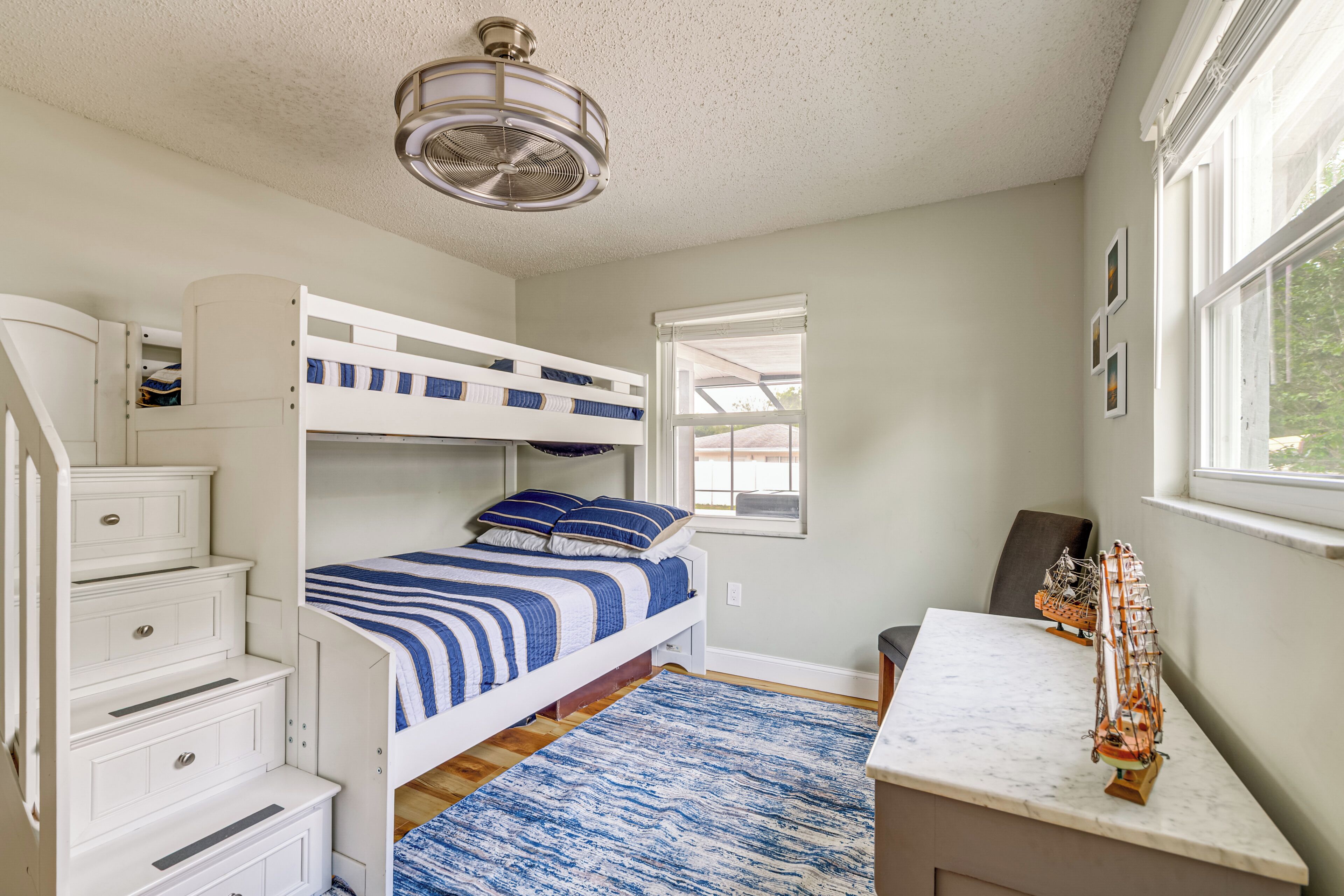 A bunk bed room with a desk, a chair, a ceiling fan, and a window.