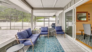 Un patio techado con un tapete azul estampado, un sofá, dos sillones, una mesita y una mesa de comedor con sillas.