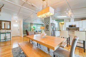 Ein geräumiges Wohnzimmer mit einem Holzesstisch, bequemen Sitzgelegenheiten, einer Kristallleuchtre und einer Küchenzeile mit modernen Geräten.