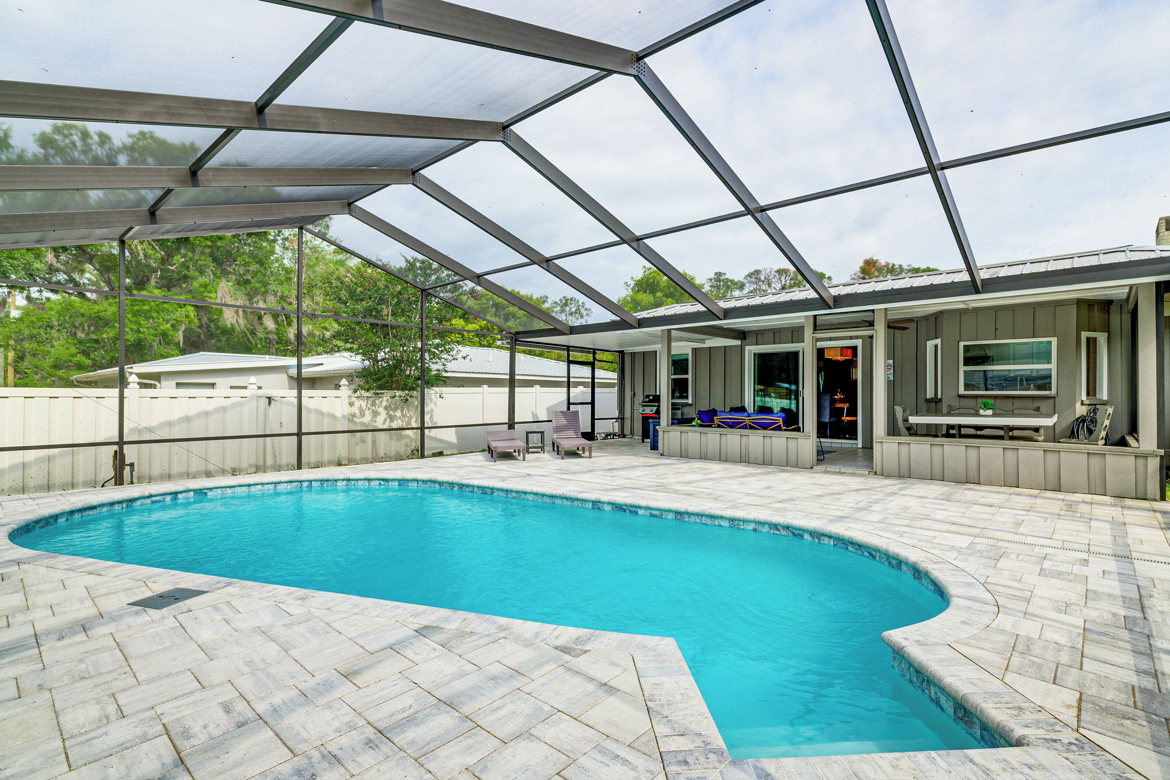 A swimming pool with a covered patio area, outdoor seating, and a view of the surrounding landscape.
