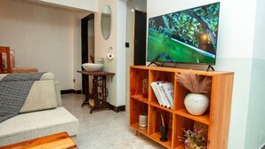 A living room with a TV, wooden shelves, a sofa, a coffee table, and a small table with a bowl. - Ukarimu Hosts (Arusha)