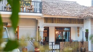 A two-story building with a thatched roof, a balcony with seating, and potted plants. - Ukarimu Hosts (Arusha)