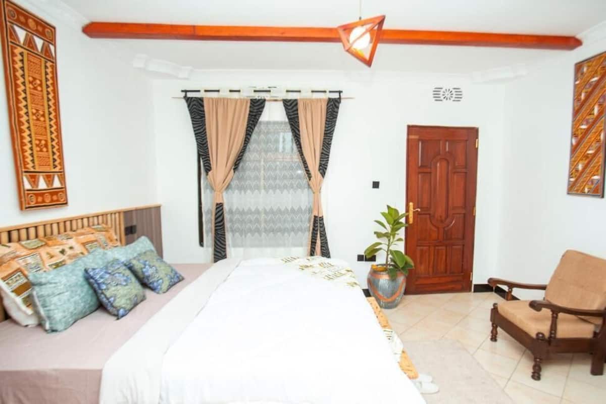 Un dormitorio con cama, una silla, una puerta y una ventana con cortinas.
