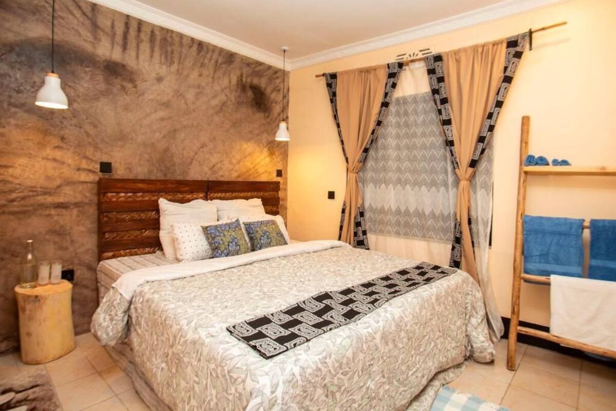 Un dormitorio con cabecera de madera, colcha estampada y ventana con cortinas decoradas.