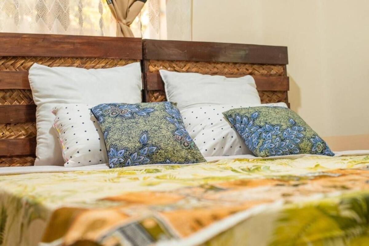 Una cama con cabecera trenzada, dos almohadas blancas y dos almohadas estampadas.