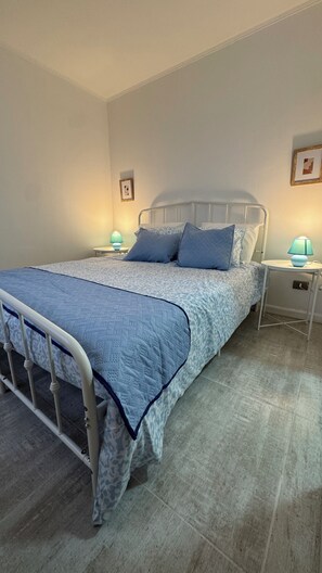 Un dormitorio con una cama, dos mesitas de noche y una mesita auxiliar, además de un cuadro colgado en la pared.