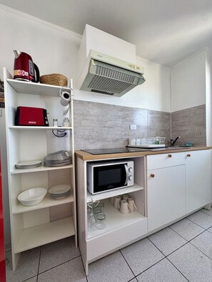 Una cocina compacta con armarios blancos, un microondas y un horno empotrado.