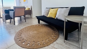 A living room with a sofa, a round woven rug, a dining area with chairs, and a wall with woven decorations. - Departamento 1501 Movistar Arena (Santiago)