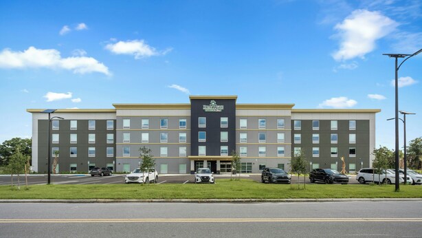 Un hotel de varios pisos con techo plano, una entrada central y un estacionamiento con varios coches.