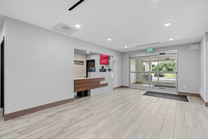 Un área de recepción con un banco, un mostrador de recepción, una puerta de cristal de entrada y un cartel que indica Wi-Fi gratuito en todas las habitaciones.