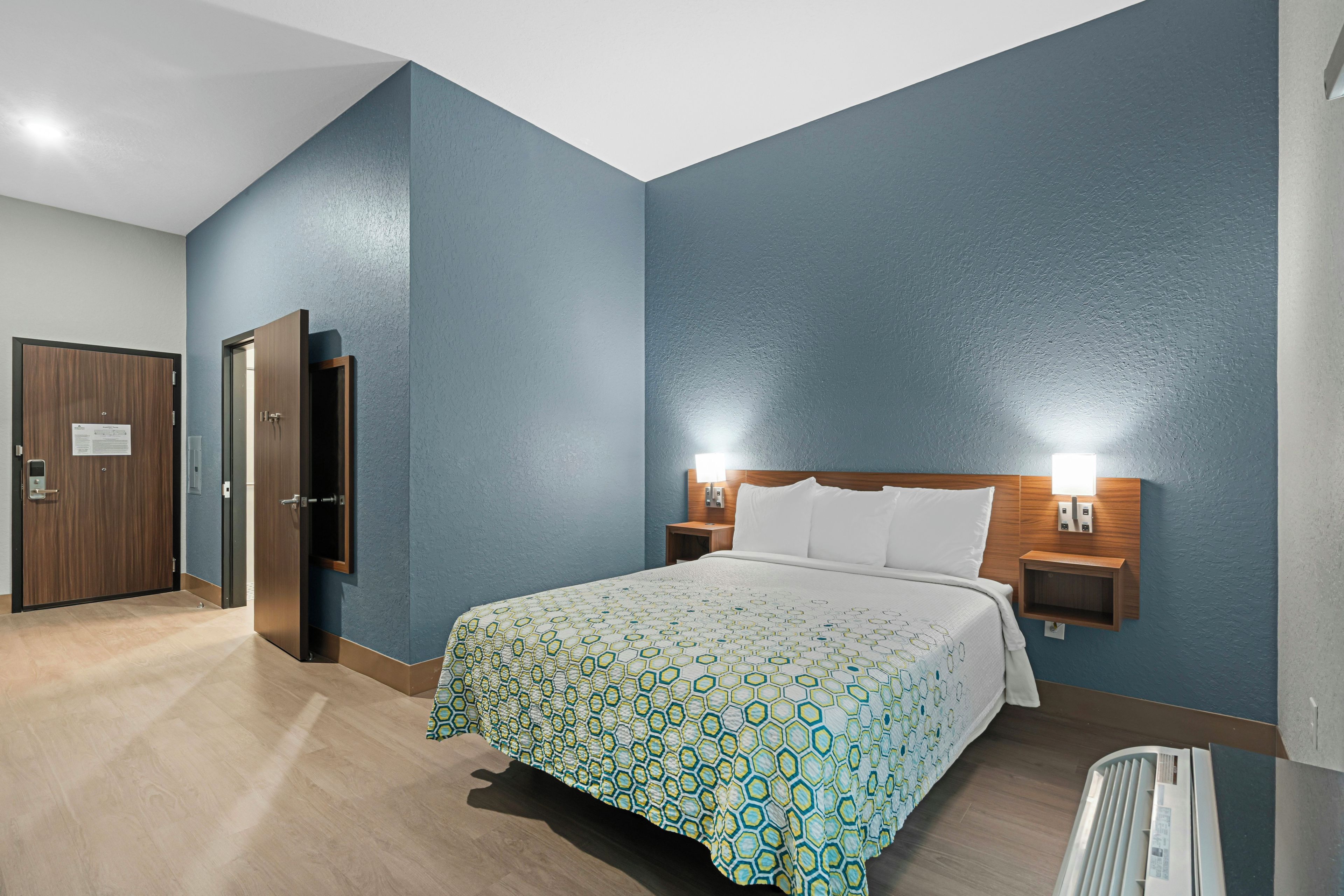 Habitació d'hotel amb un llit, taules de nit, una taula auxiliar i una làmpada penjada a la paret.