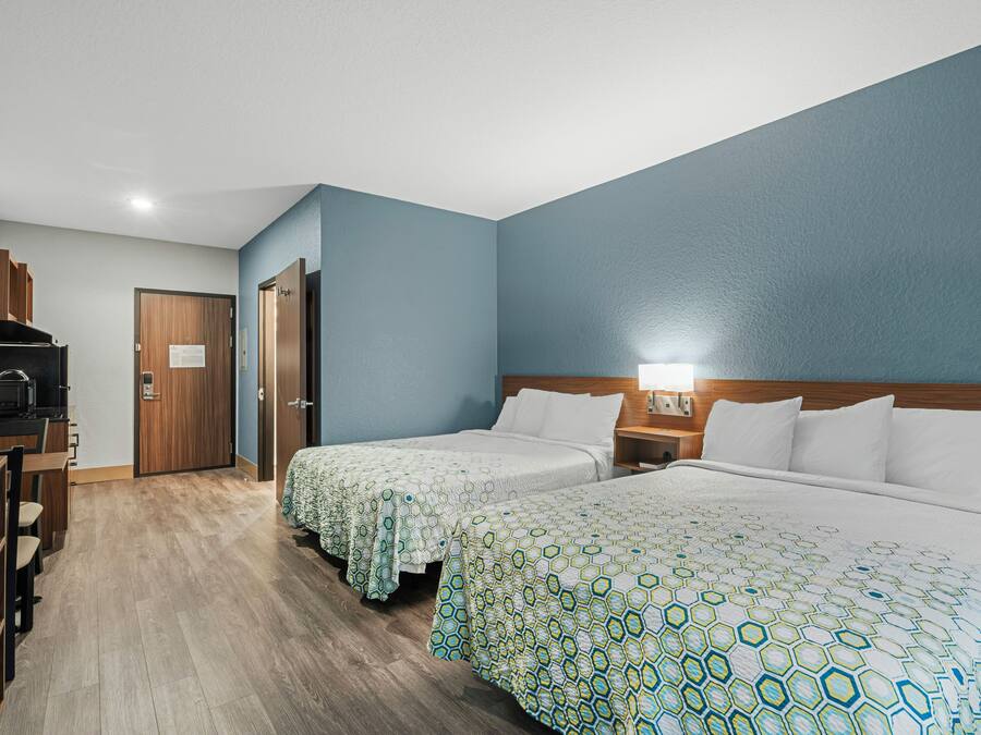 A hotel room with two beds, a kitchenette, and a wooden desk.