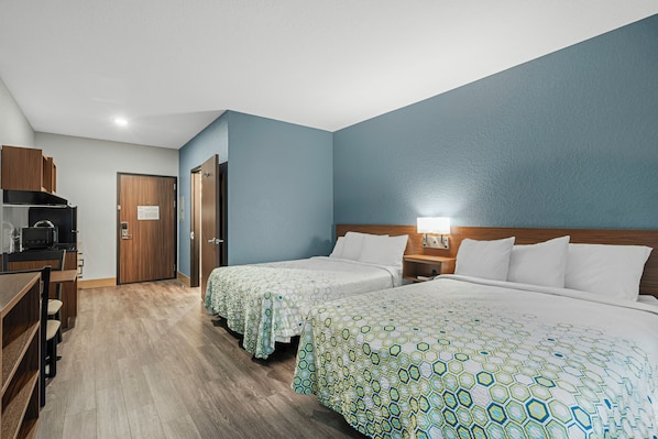 Une chambre d’hôtel avec deux lits, une kitchenette et un bureau en bois.