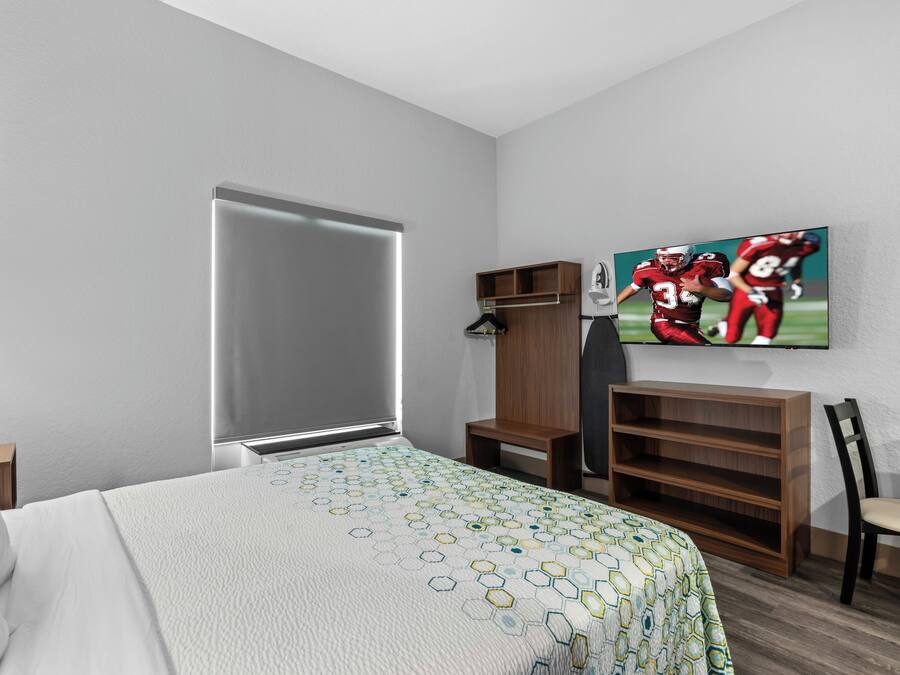 Una habitación de hotel con una cama, un armario, un televisor y un estante.
