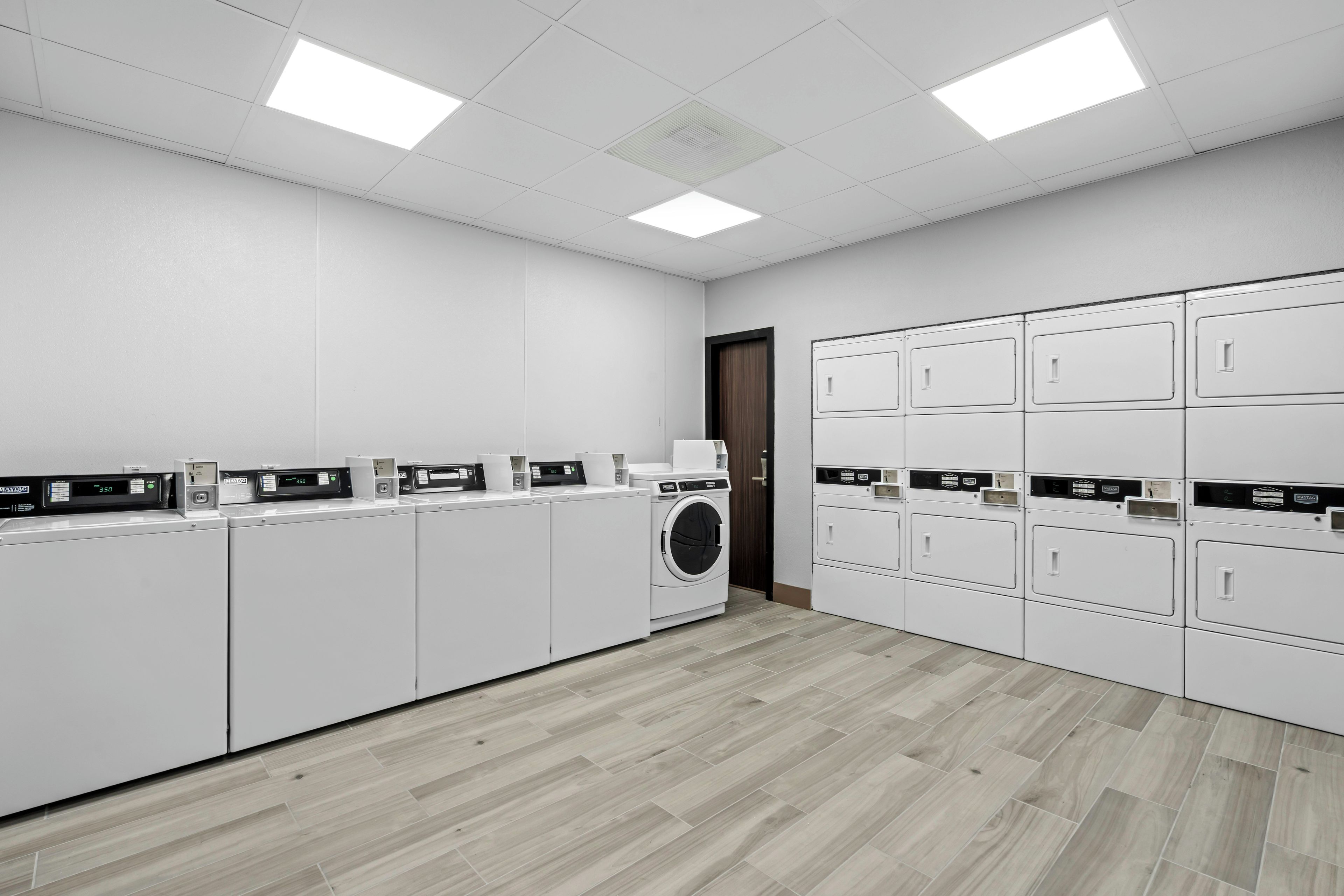 A laundry facility with multiple washing machines and dryers, a wooden floor, and a white wall.