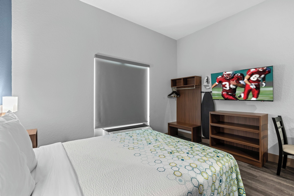 Una habitación de hotel con una cama, un armario, un televisor y un estante.