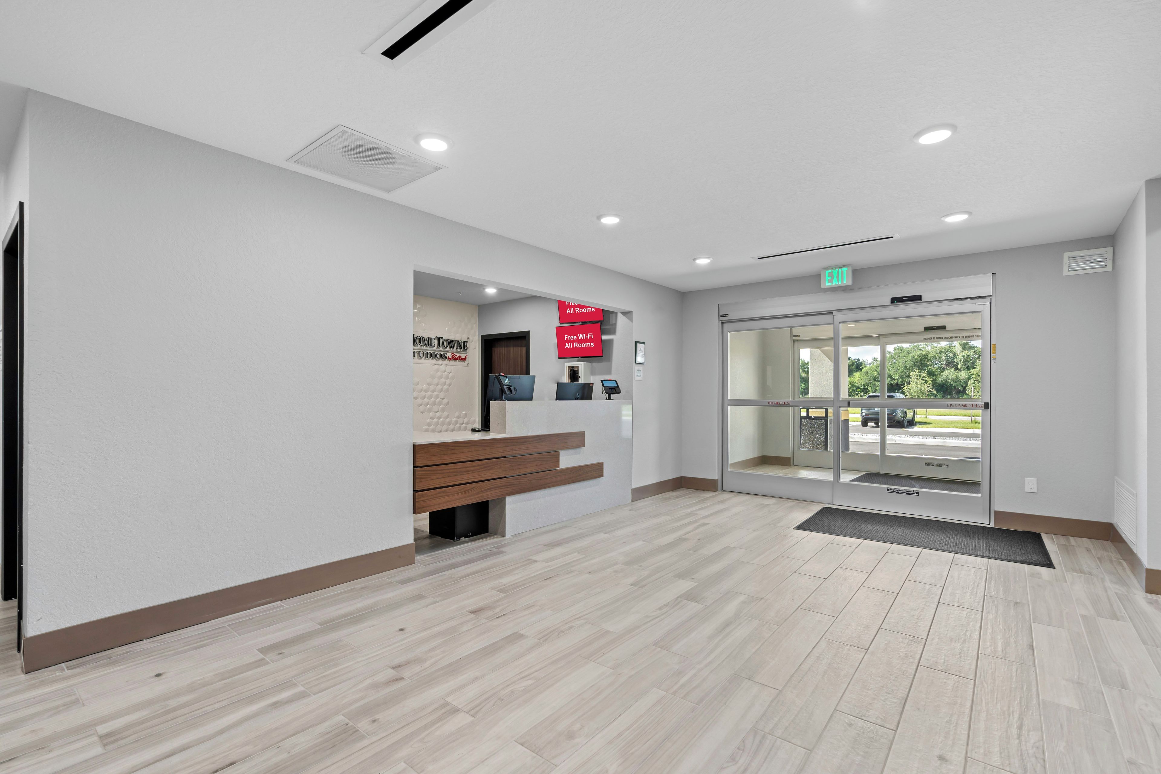 Un área de recepción con un banco, un mostrador de recepción, una puerta de cristal de entrada y un cartel que indica Wi-Fi gratuito en todas las habitaciones.