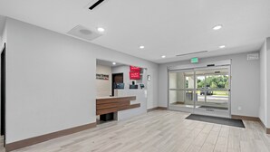 Un área de recepción con un banco, un mostrador de recepción, una puerta de cristal de entrada y un cartel que indica Wi-Fi gratuito en todas las habitaciones.