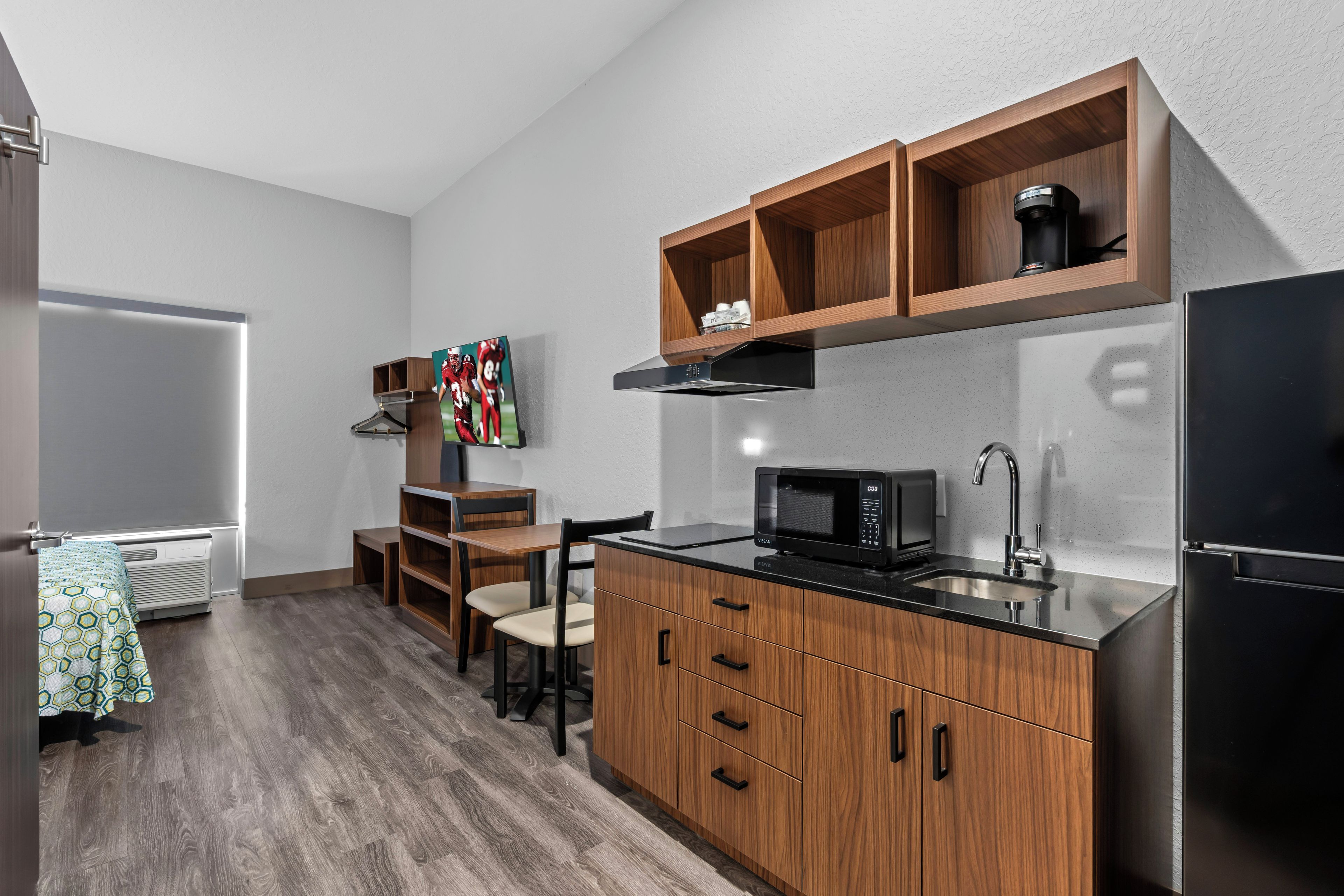 A compact kitchen with wooden cabinets, a microwave, and a coffee maker on a shelf.