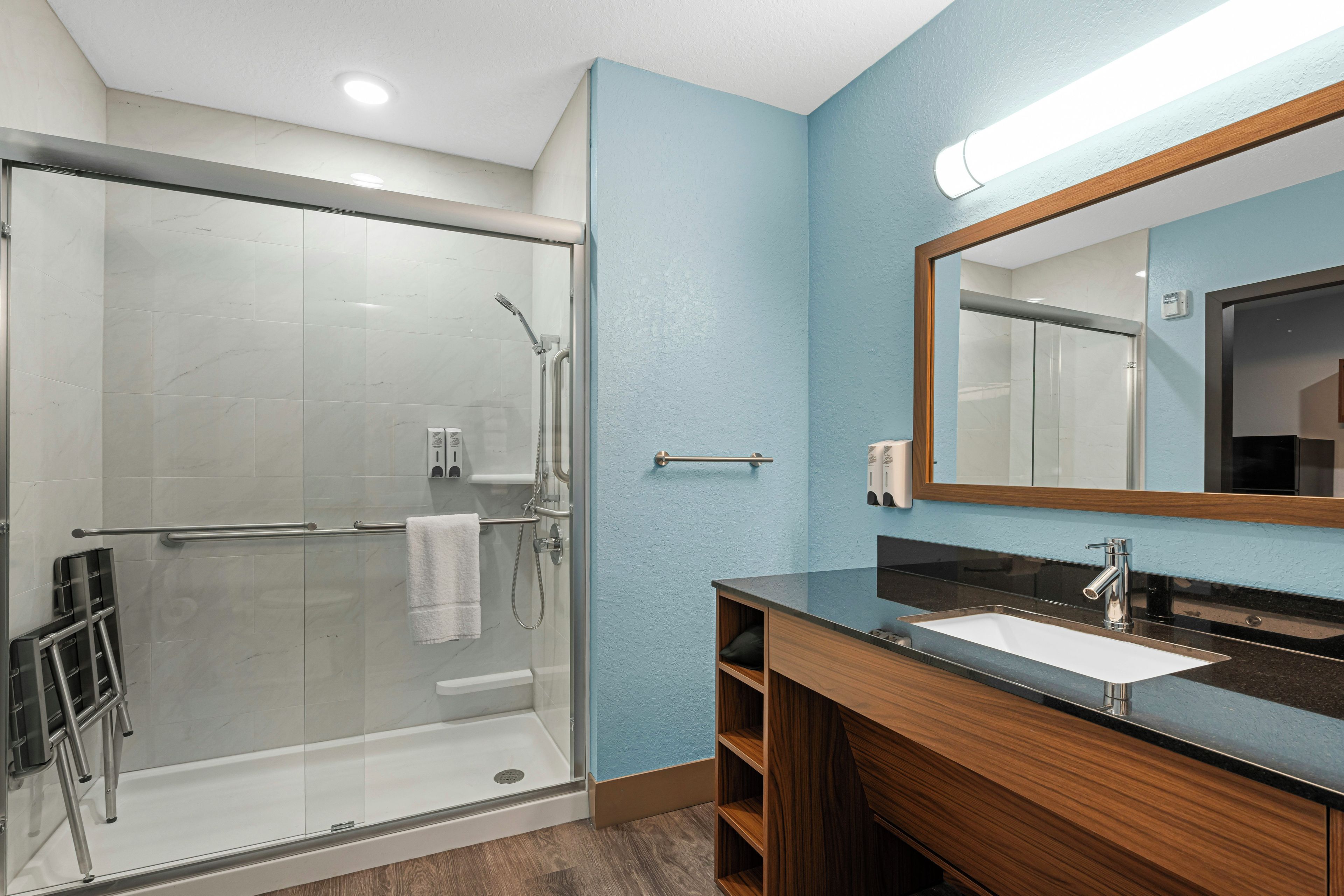 Un baño moderno con ducha de vidrio, tocador de madera con lavamanos y un espejo grande.