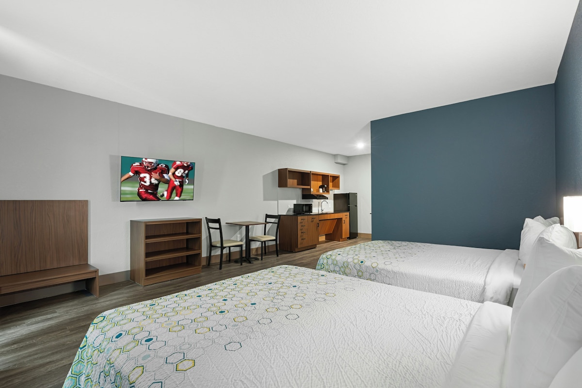 Habitación de hotel con dos camas, un escritorio, una silla, un televisor y una kitchenette.