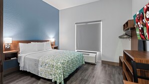 Una habitación de hotel con cama, mesitas de noche, armario, escritorio y un ventanal grande.