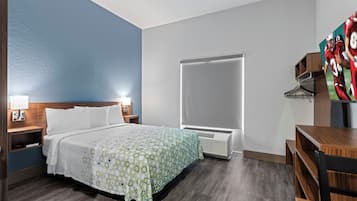 Una habitación de hotel con cama, mesitas de noche, armario, escritorio y un ventanal grande.