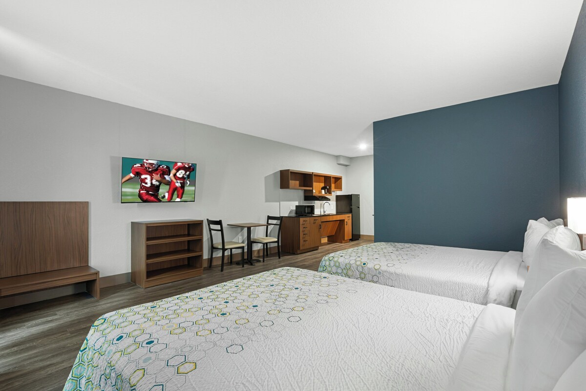 Une chambre d’hôtel avec deux lits, un bureau, une chaise, une télévision et une kitchenette.