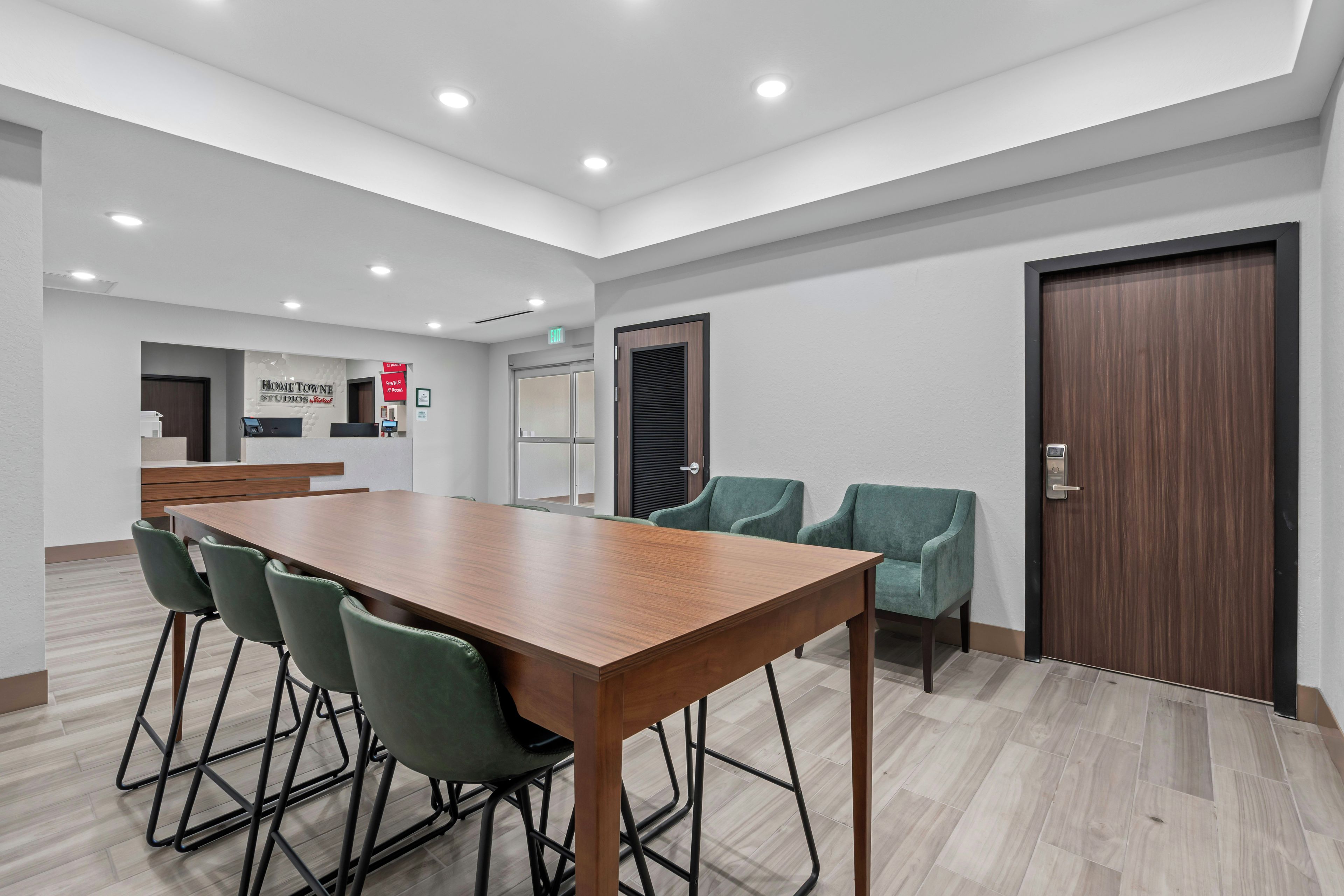 Uma sala de conferências com uma mesa comprida e quatro cadeiras, um balcão de recepção e uma porta com fechadura eletrônica.