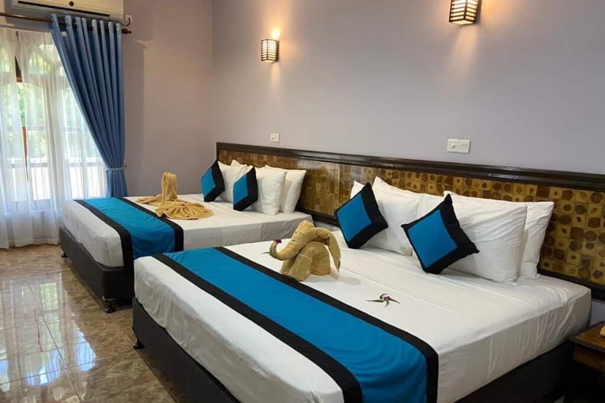 A hotel room with two beds, each with a blue and black bedspread, white pillows, and a headboard with a patterned design.
