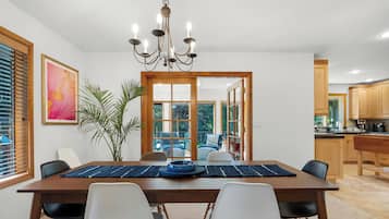 Comedor con una mesa, sillas, una lámpara de araña, una planta y vistas a través de un ventanal.