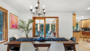 Ein Essbereich mit Tisch, Stühlen, einer Chandelierleuchte, einer Pflanze und Blick durch eine Glastür.