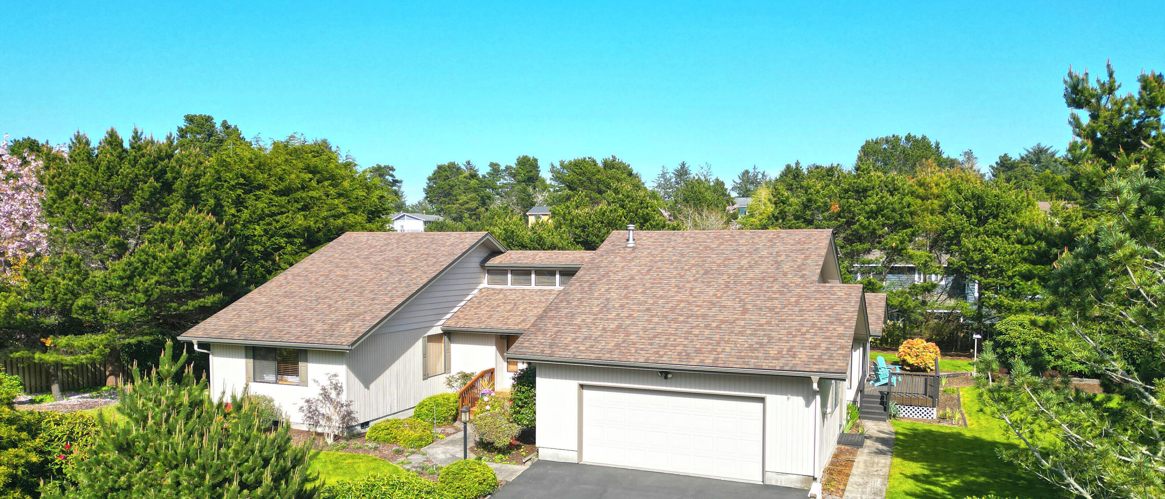 Une maison à deux étages avec un garage, entourée d’une végétation luxuriante et d’arbres.