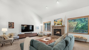 Ein Wohnzimmer mit Flachbildfernseher, Kamin und großen Fenstern.