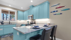 A modern kitchen with teal cabinetry, a central island, and a dining area. - Mac's Surf Shack at Seaside Beach (Seaside)