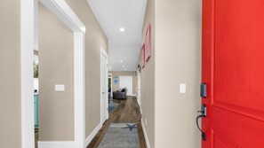 A hallway with a red door, beige walls, and a wooden floor. - Mac's Surf Shack at Seaside Beach (Seaside)